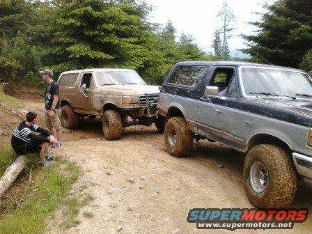 1989 Ford Bronco and another Ford Bronco on a dirt road with trees in background