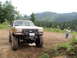 1989 Ford Bronco - A lifted Ford truck is parked on a dirt road with a wooded mountainside in the background.