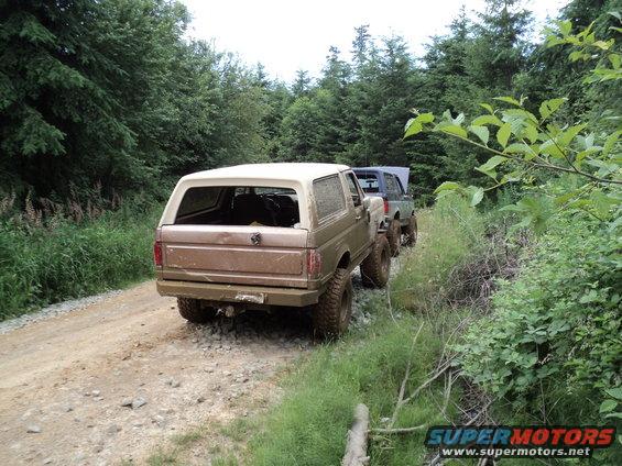 Rear view of a tan 1989 Ford Bronco on a dirt road with a blue SUV behind it