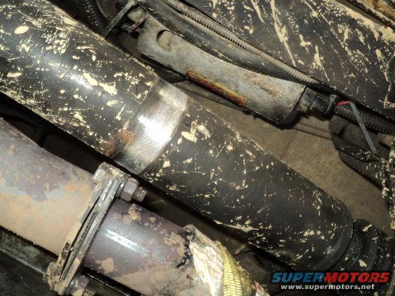 close-up of driveshaft and exhaust pipes, covered in mud splatters. A Supermotors.net watermark is visible