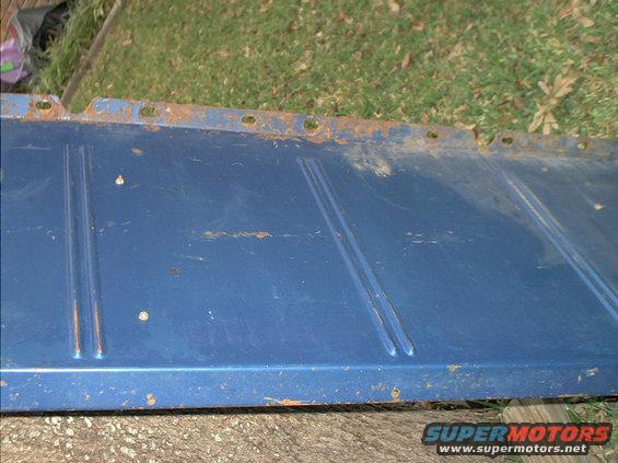 Blue metal panel with some rust around the edges and holes. It has two raised lines running down its length