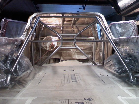 Roll cage inside a vehicle, covered in plastic sheeting, with paper on the floor