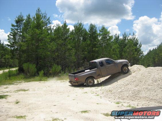Gray pickup truck driving up a dirt pile, side view