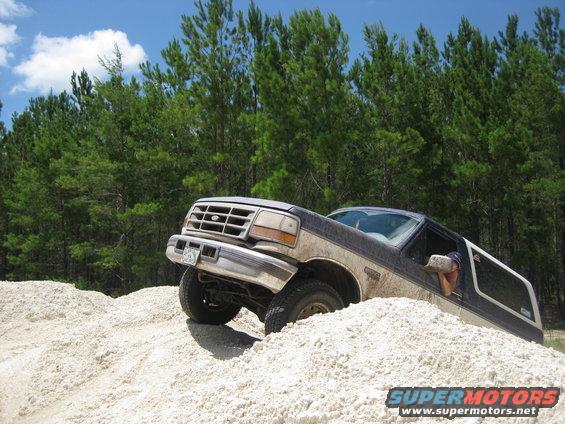 1994 Ford Bronco climbing a sand dune with trees in the background