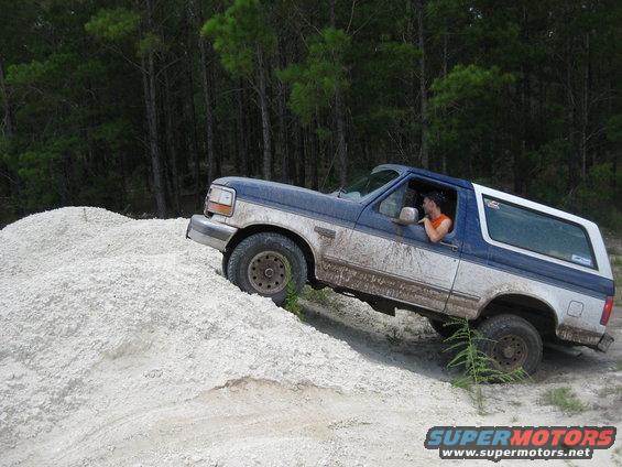 Blue and white Ford Bronco driving up a sandy hill, driver visible