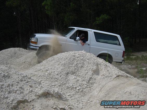 White Ford Bronco driving through a sand pile, kicking up dust