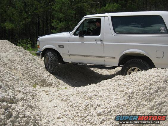White 1994 Ford Bronco driving over a pile of light-colored dirt