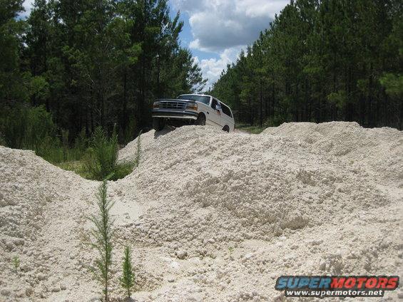 1994 Ford Bronco driving up a dirt mound with trees in the background