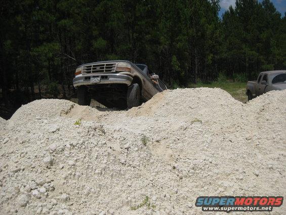 1994 Ford Bronco climbing over dirt mounds with another truck in the background