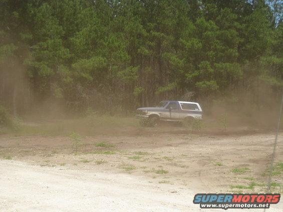 1994 Ford Bronco kicking up dust while driving on a dirt road near trees