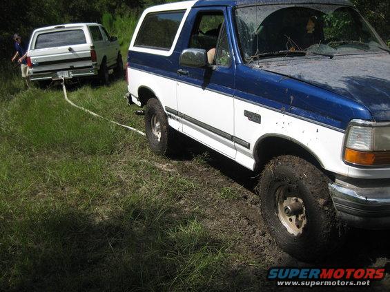 1994 Ford Bronco stuck in mud, being towed by another Ford Bronco
