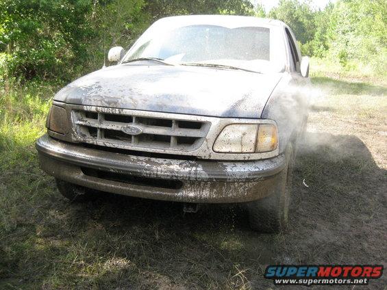 Front view of a mud-splattered 1997 Ford F-150 driving through mud
