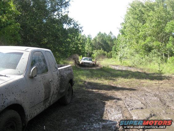Muddy pickup truck in foreground, another truck splashing through mud puddle in background