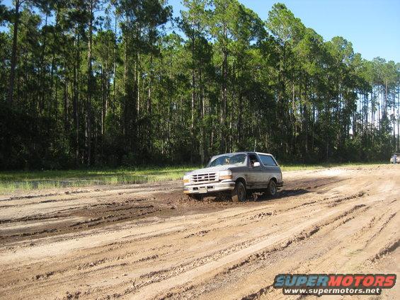 Ford Bronco driving through mud with trees in background