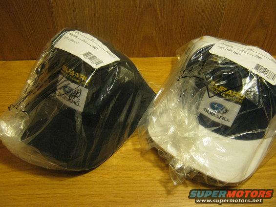 Two Subaru rally team hats in plastic packaging, one black, one white and blue