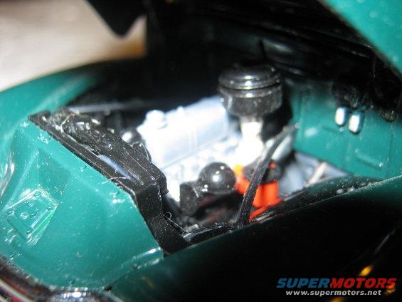Model car engine bay with silver engine block, black air filter housing, and orange spark plug wires