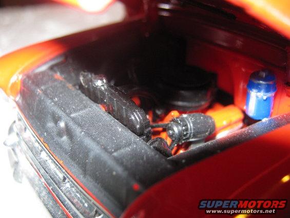Engine bay of a red vehicle with orange engine block and blue fluid canister