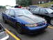 1992 Ford Taurus - A blue 1992 Ford Taurus with a custom hood is parked next to other vehicles at an outdoor gathering.