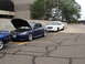1992 Ford Taurus - Two sedans, one blue with its hood up, are parked in a lot with cracked pavement.
