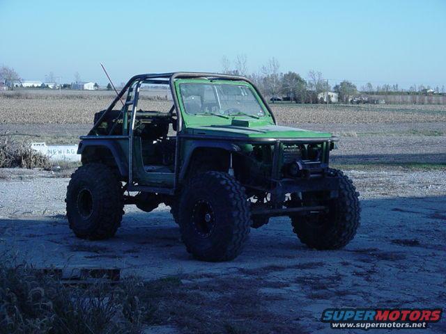 Green off-road vehicle with large tires and a roll cage, parked outdoors