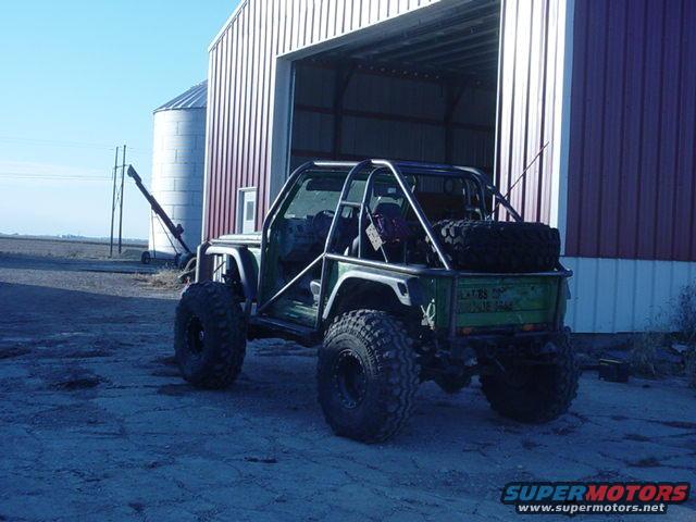 Green off-road SUV with custom roll cage and large tires parked in front of a barn