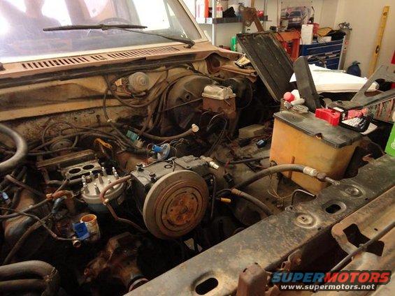 Engine bay with carburetor, distributor, and AC compressor visible. Wires and hoses are present