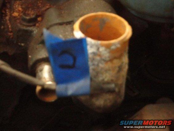 Close-up of an engine part, possibly a hose fitting, with blue tape marked with a 'U'