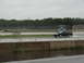 1992 Ford Taurus - A dark sedan drives on a wet track under an overcast sky, with another vehicle visible in the background.