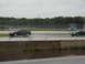 1992 Ford Taurus - Two cars drive on a wet track under an overcast sky, with a white utility vehicle visible in the distance.
