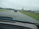 1992 Ford Taurus - A dark sedan navigates a wet racetrack under an overcast sky.