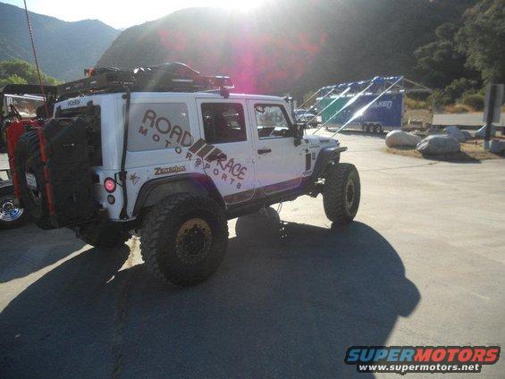White Jeep Wrangler with 'Road Race Motorsports' graphics, spare tire on rear, roof rack