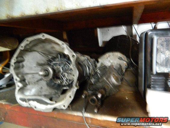 Two disassembled transmission components on a wooden shelf, one with an open bell housing