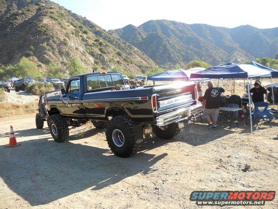 Black lifted Ford F-Series truck, 1973 model year, seen from a 3/4 front angle with large off-road tires