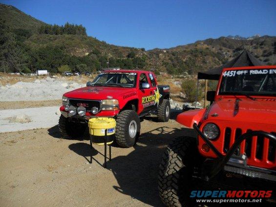 Red GMC pickup truck with large tires and Rockstar decals parked next to an orange Jeep