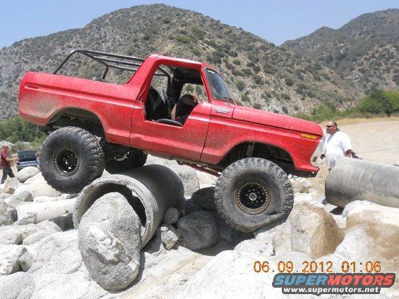 red Bronco climbing over rocks and concrete pipes, roll cage installed