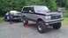 1973 Ford Torino - A lifted Ford Bronco tows a 1975 Ford car on a trailer, with a person standing nearby.