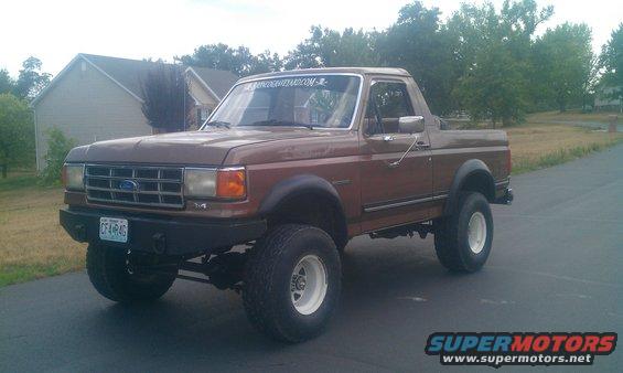 Brown 1987 Ford Bronco with lifted suspension and white rims parked on asphalt