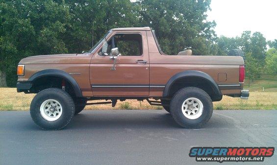 Brown 1987 Ford Bronco lifted with white wheels, seen from the side