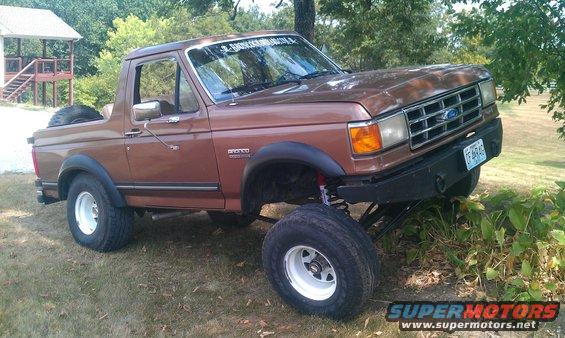 1987 Ford Bronco lifted with large off-road tires, aftermarket bumper, and spare tire on the back