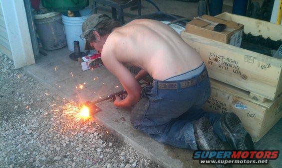 Person welding on concrete with sparks flying, wearing jeans and a hat
