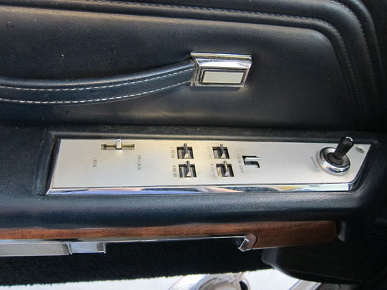 Car door panel with chrome trim, black upholstery, wood accent, and power window switches labeled 'LOCK', 'ON-LOCK', 'REAR', 'FRONT', and 'LOW LOCK'