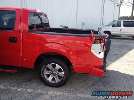 Red pickup truck with damaged rear bumper and taillight. A silver van is parked behind it