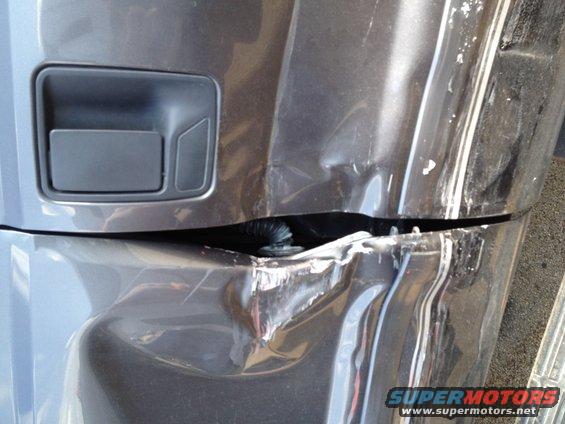 Dark gray truck bumper with significant damage, showing a dented section and a detached panel near the door handle