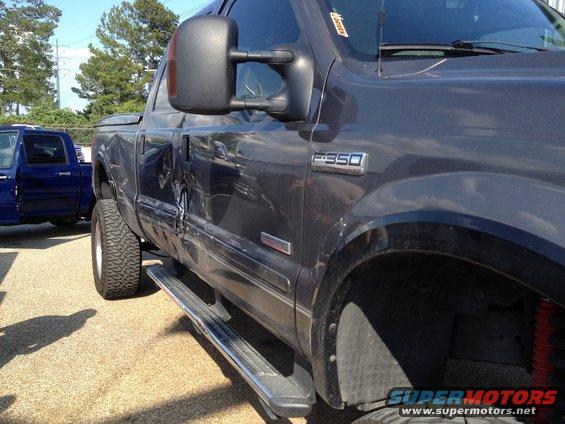 Side view of a dark gray 2006 Ford F-350 truck with a blue truck parked nearby