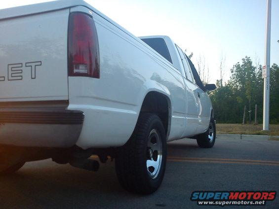 Rear quarter view of a white pickup truck. The taillight and part of the tailgate are visible