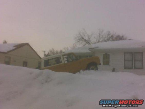 1966 Ford Bronco partially buried in snow next to a house