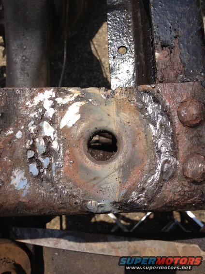 Close-up of a heavily rusted vehicle frame section with a circular hole and visible welds