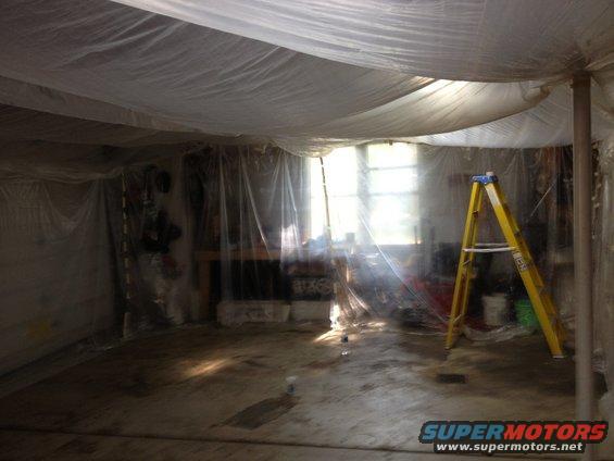 Interior of a room covered in plastic sheeting with a yellow ladder and windows
