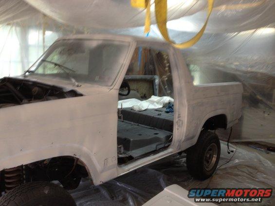 Ford Bronco with doors open, stripped down and covered in primer, inside a plastic-covered paint booth