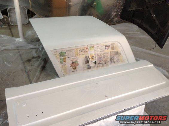 White car door and hood covered in newspaper, inside a workshop